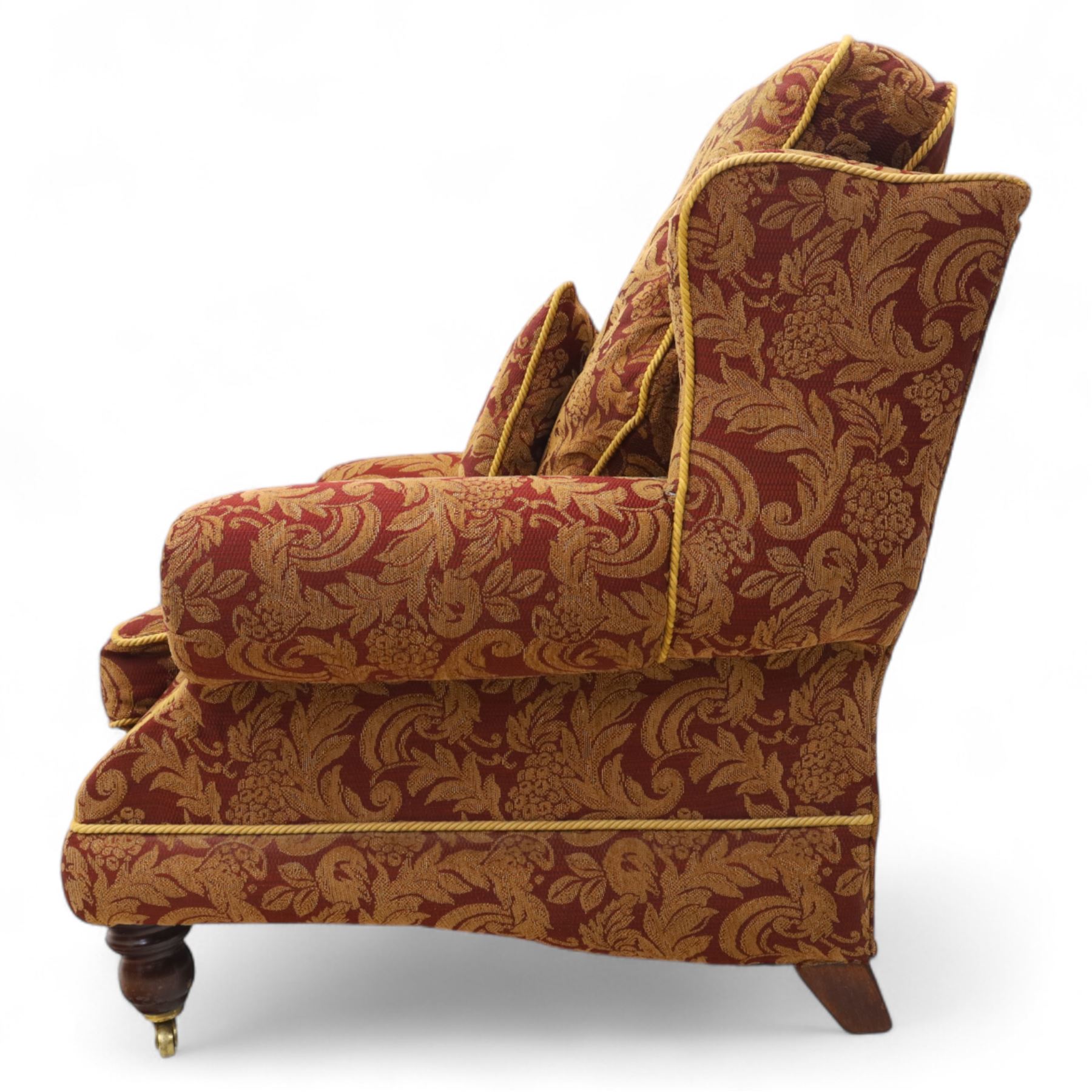 Duresta – pair of armchairs, upholstered in red and gold damask fabric with piped edges, scroll arms and loose feather-filled cushions, raised on turned wooden feet with brass castors