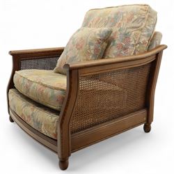 Ercol – bergère four piece suite, including armchair, two seat sofa, three seat sofa and footstool, all with removable floral upholstered cushions, the frames with side caning and rounded arm supports in stained beech

Three seat (H 87cm, D 89cm, W 196cm)
Two seat (H 87cm, D 89cm, W 137cm)
Armchair (H 87cm, D 89cm, W 87cm)
Footstool (H 28cm, D 55cm, W 55cm)