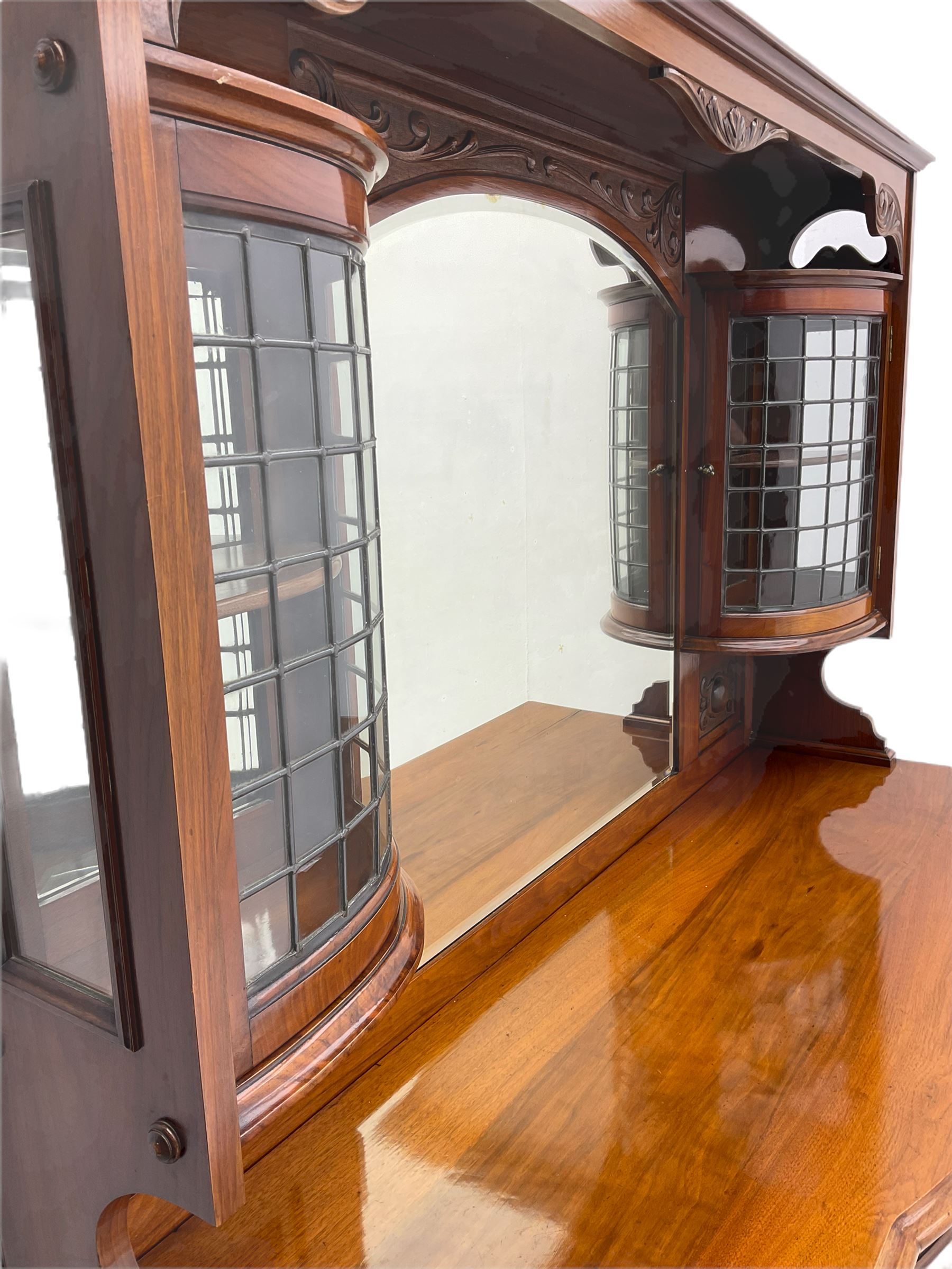 Late Victorian walnut mirror back sideboard or dresser, the raised back fitted with two curved and lead glazed cabinets, central arched bevelled mirror, the sideboard with break bowfront, fitted with six drawers and two cupboards, the cupboard doors panelled and carved with scrolls, shell and plant motifs, shaped apron with cabriole feet
