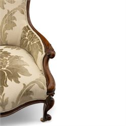 Victorian mahogany framed spoon back armchair, the shaped and padded back over serpentine seat upholstered in a floral damask pattern fabric within a moulded frame carved with scrolled arms, raised upon cabriole front legs with scroll feet on porcelain castors 