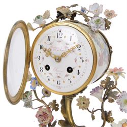 French- early 20th century 8-day Chinoiserie brass and porcelain mantel clock in the 18th century style, brass base with splayed feet profusely decorated with clusters of painted porcelain flowers and two decoratively painted Chinese foo dogs, movement enclosed in a circular porcelain movement case illustrated with birds of paradise and oriental motifs, with a white enamel dial Arabic numerals, minute markers, pierced gilt hands and a floral swag, rack striking Parisian movement striking the hours and half-hours on a bell. With a visible sunburst pendulum and key.
