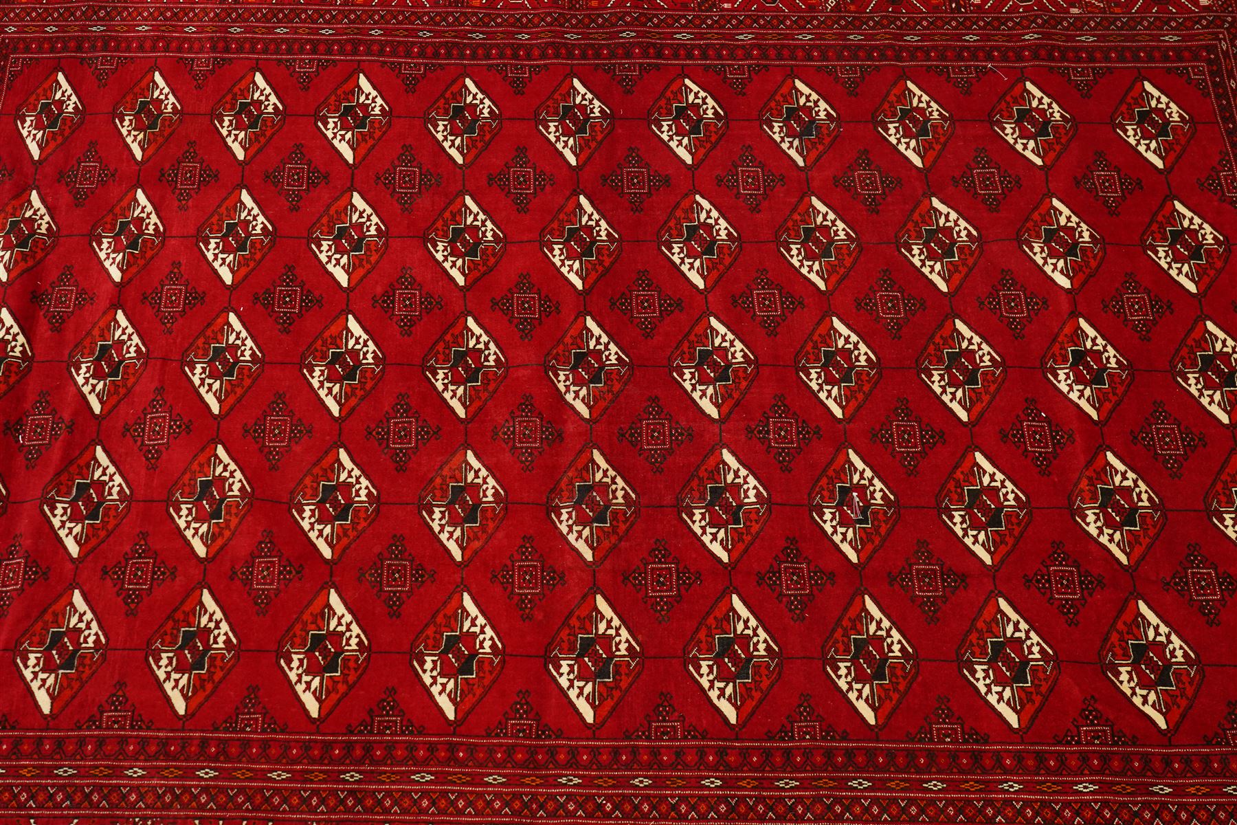 Turkmen hand-knotted carpet, deep crimson ground field, with an all-over lattice of repeating diamond guls, each enclosing angular cruiform motifs, and stylized tribal devices, interspersed with smaller geometric ornaments, main border decorated with repeating geometric motifs and stylized tribal elements, flanked by narrow guard stripes, with cotton fringe ends 
