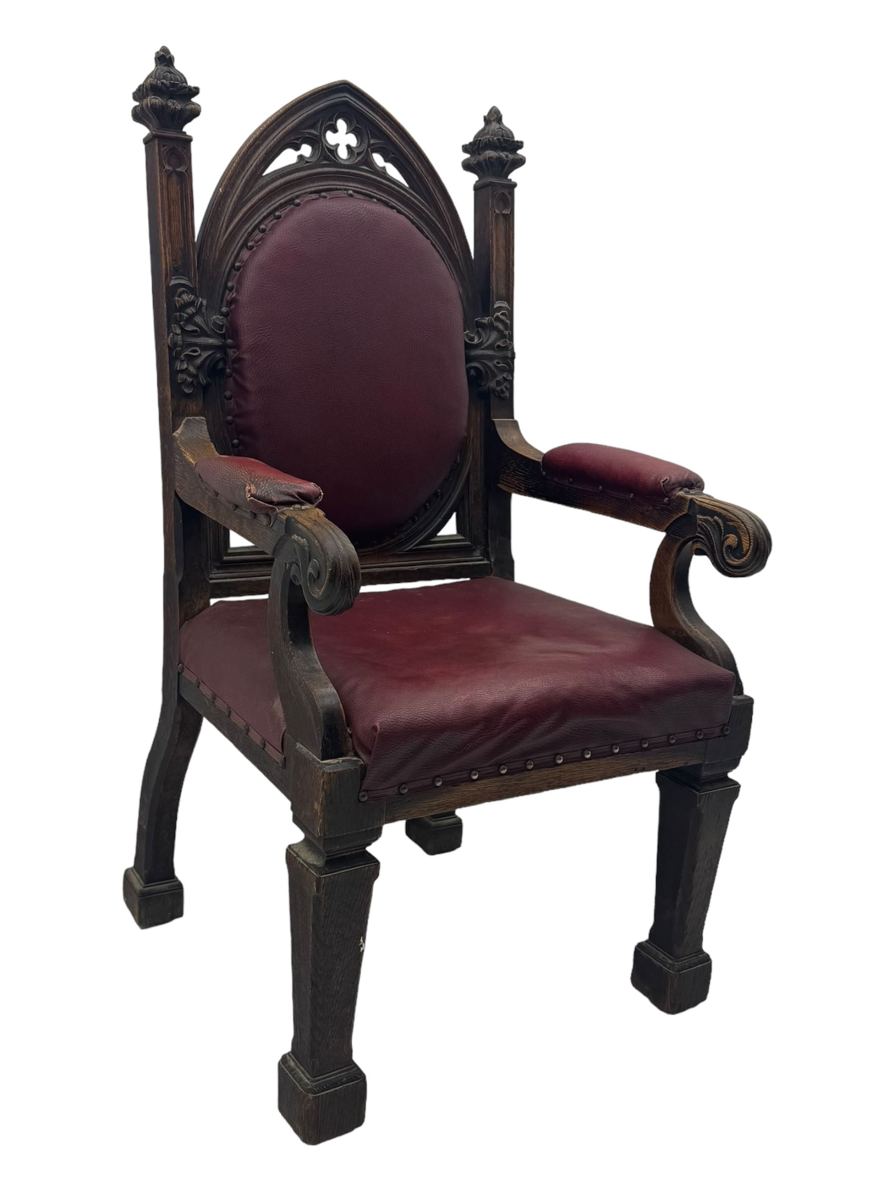 Late Victorian Gothic-revival armchair, arched crest rail carved with tracery and trefoil detail, padded circular back and seat, brass studded burgundy leather upholstery, shaped armrests with scrolled terminals, on square tapering supports
