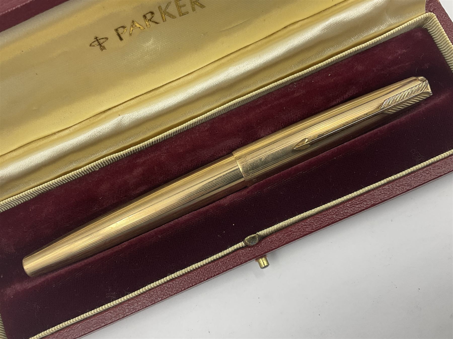 Three rolled gold Parker fountain pens, comprising an example with a gold nib marked 14K 585 and barrel with a shell stamp, a Parker 61 fountain pen with inset gold arrow to the nib, and another similar, all with striated decoration and arrow clips to the caps, L13cm, one with box