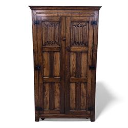 Mid 20th century oak double wardrobe, the rectangular top above twin panelled doors with carved linenfold decoration and wrought iron hinges, raised on block feet