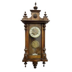 German - late 19th century spring driven wall clock in a walnut and ebonised case, with a fully glazed door and decorative pediment with turned finials, ivorine chapter with Roman numerals and an embossed gilt dial centre, with a repousse pendulum bob and beat plate, twin train movement striking the hours on a coiled gong.