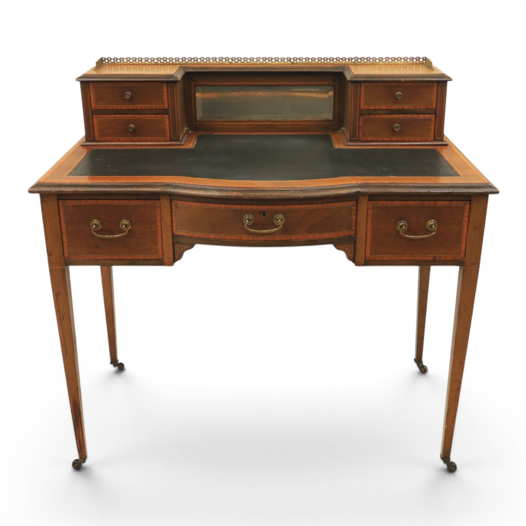 Maple & Co - Edwardian mahogany inlaid writing desk, the superstructure with pierced brass gallery, above an inset mirror and two short drawers, inset leather writing surface, bow fronted with crossbanded drawers and brass swan neck handles, square tapering supports terminating in castors 