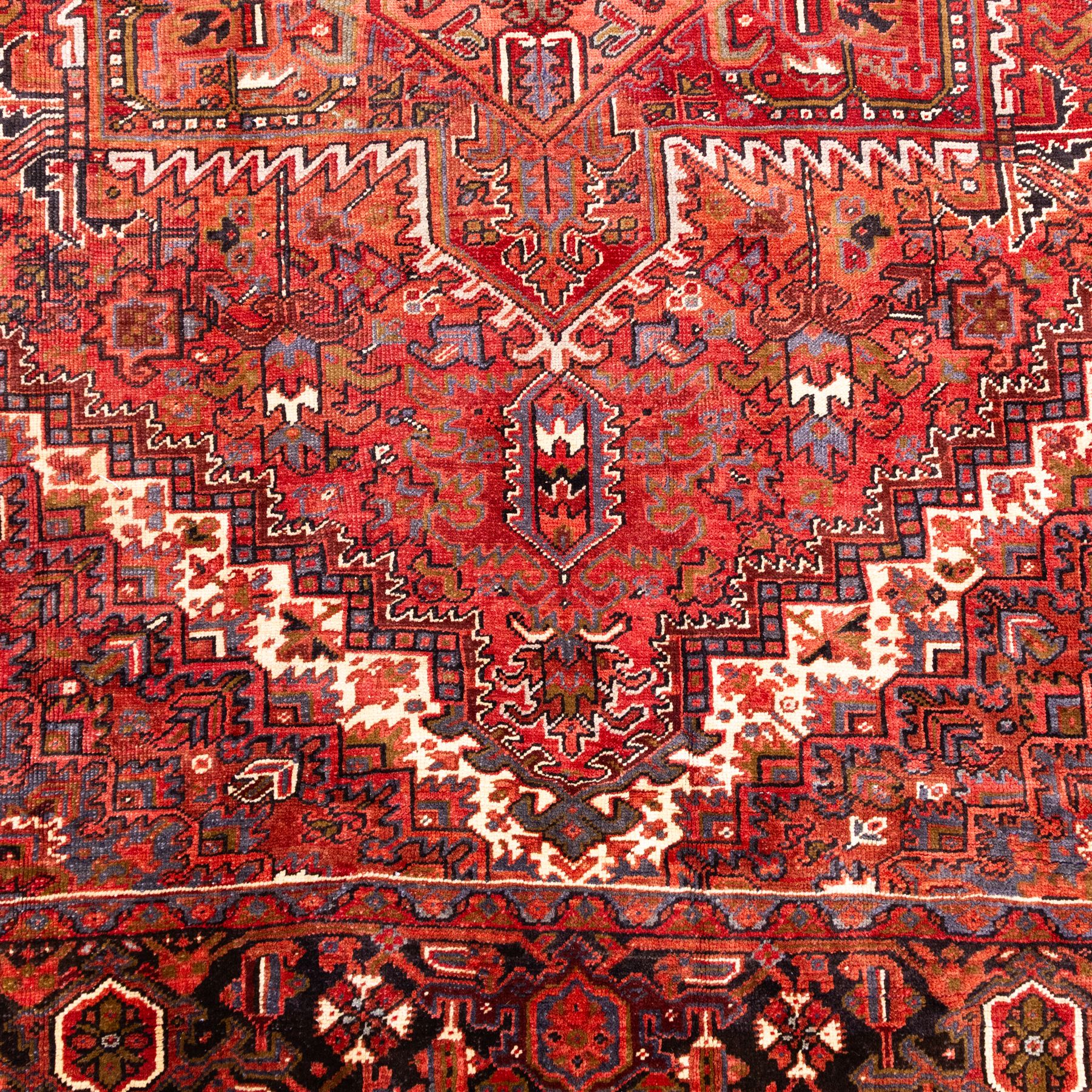 North West Persian Heriz hand-knotted carpet, madder red field, with a large central angular star medallion with stepped outlines on ivory ground, surrounded by geometric floral devices and stylized rosettes, with corresponding corner spandrels, enclosed by a bold geometric main border with multiple guard stripes, with cotton fringe ends 