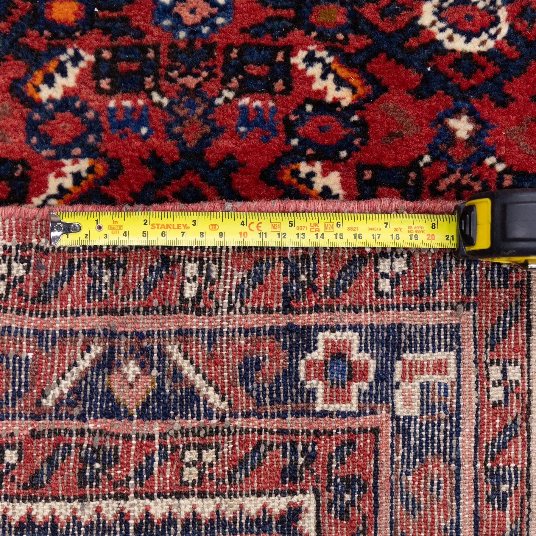 North West Persian Malayer hand-knotted runner, decorated with a dense all-over pattern of small repeating boteh and rosette motifs on a rich madder red ground, field filled with geometric floral elements arranged in a lattice design, framed by a narrow main border and flanked by slender guard borders, with cotton fringe ends 