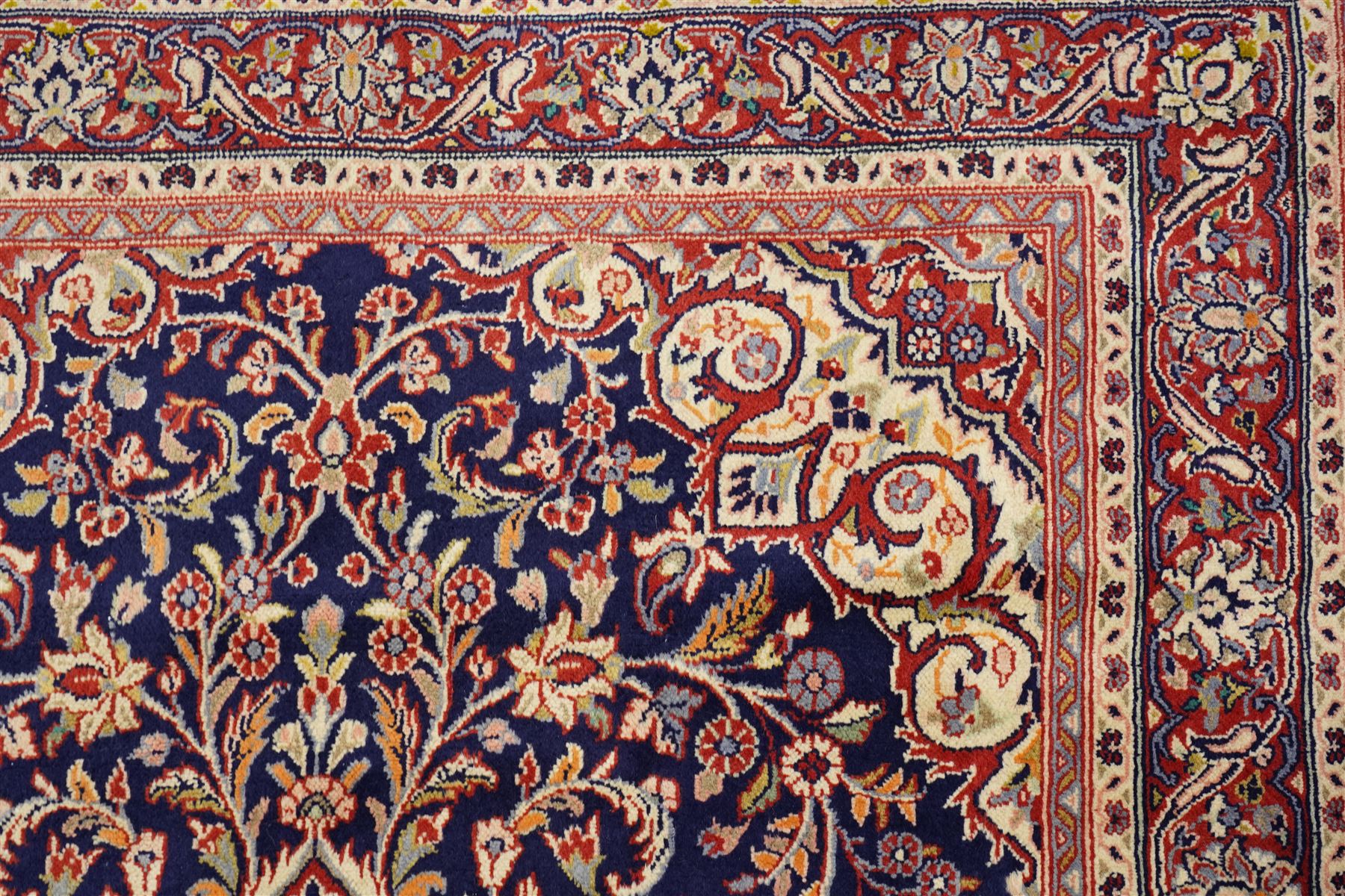 Central Persian Kashan hand-knotted rug, indigo field with central lobed medallion with pendants issuing scrolling arabesque of palmettes, flowering vines, and foliate tendrils, with conforming spandrels, with vine border and framed by guard stripes in tones indigo, ivory and madder red, with cotton fringe ends 