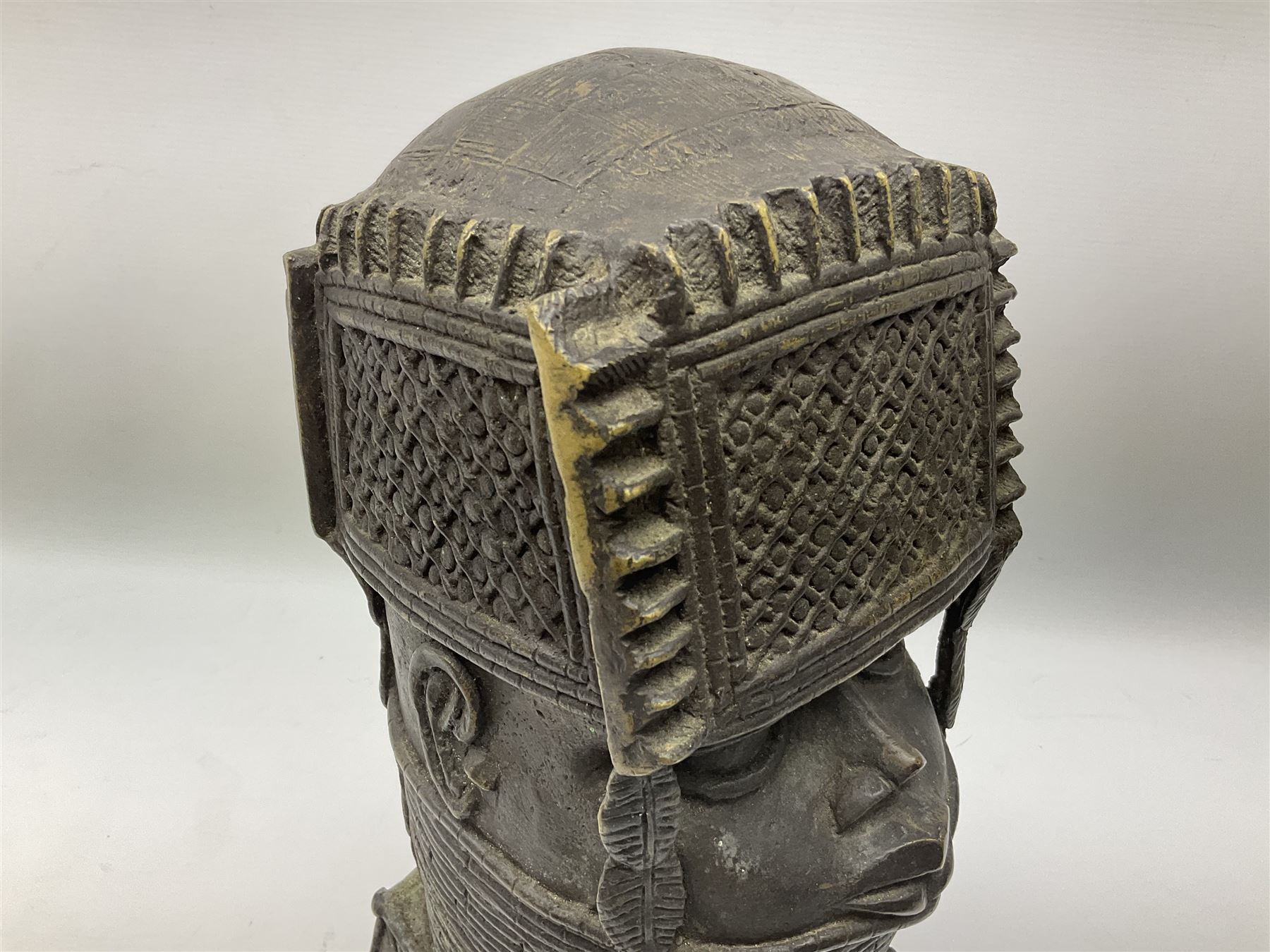 20th century Benin bronze head of an Oba, donning headdress and neck rings with wide open eyes, raised upon a tapering square base, the sides with relief cast knot decoration, H39cm