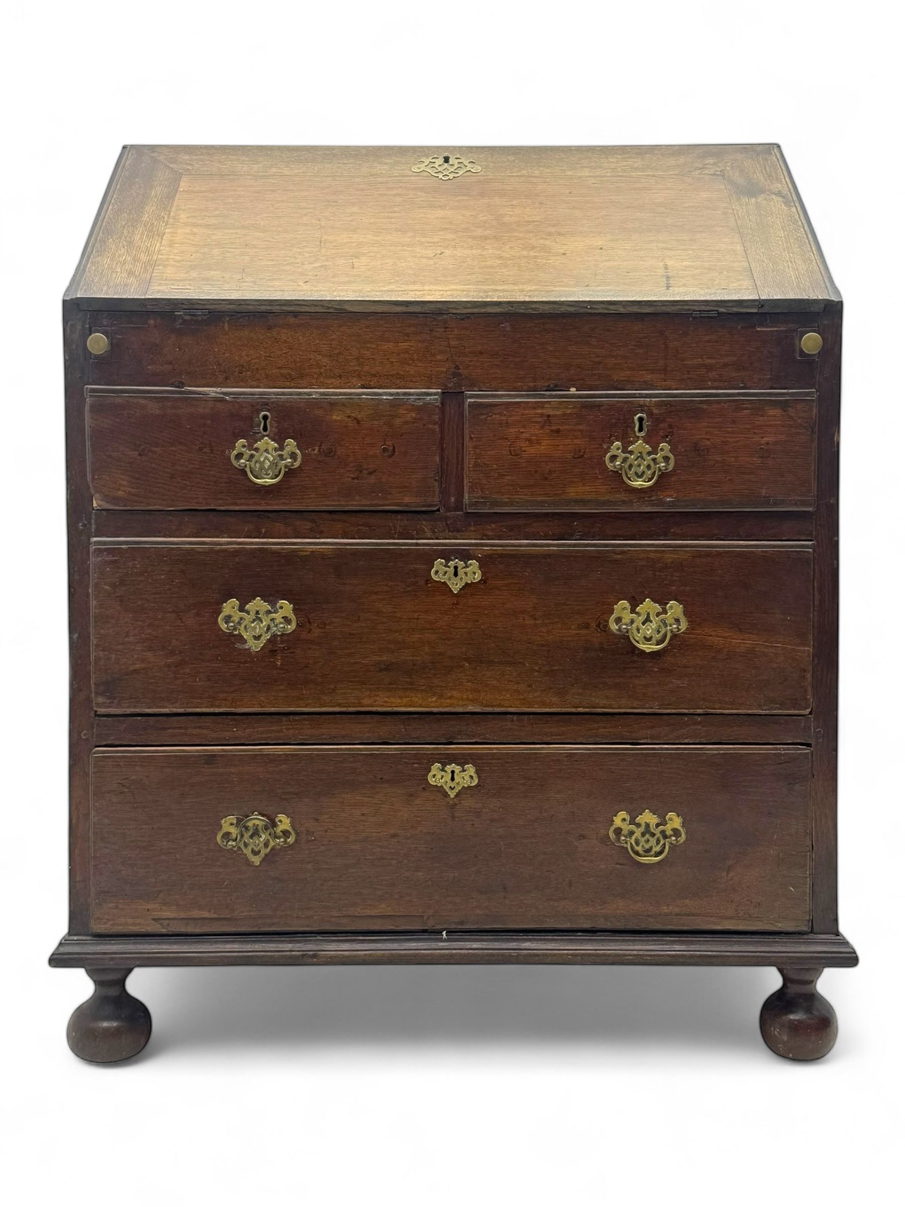 George III oak bureau, sloped fall-front enclosing a fitted interior with pigeonholes, small drawers, and a central compartment, over two short and two long drawers, brass escutcheons and drop handles, raised on bun feet