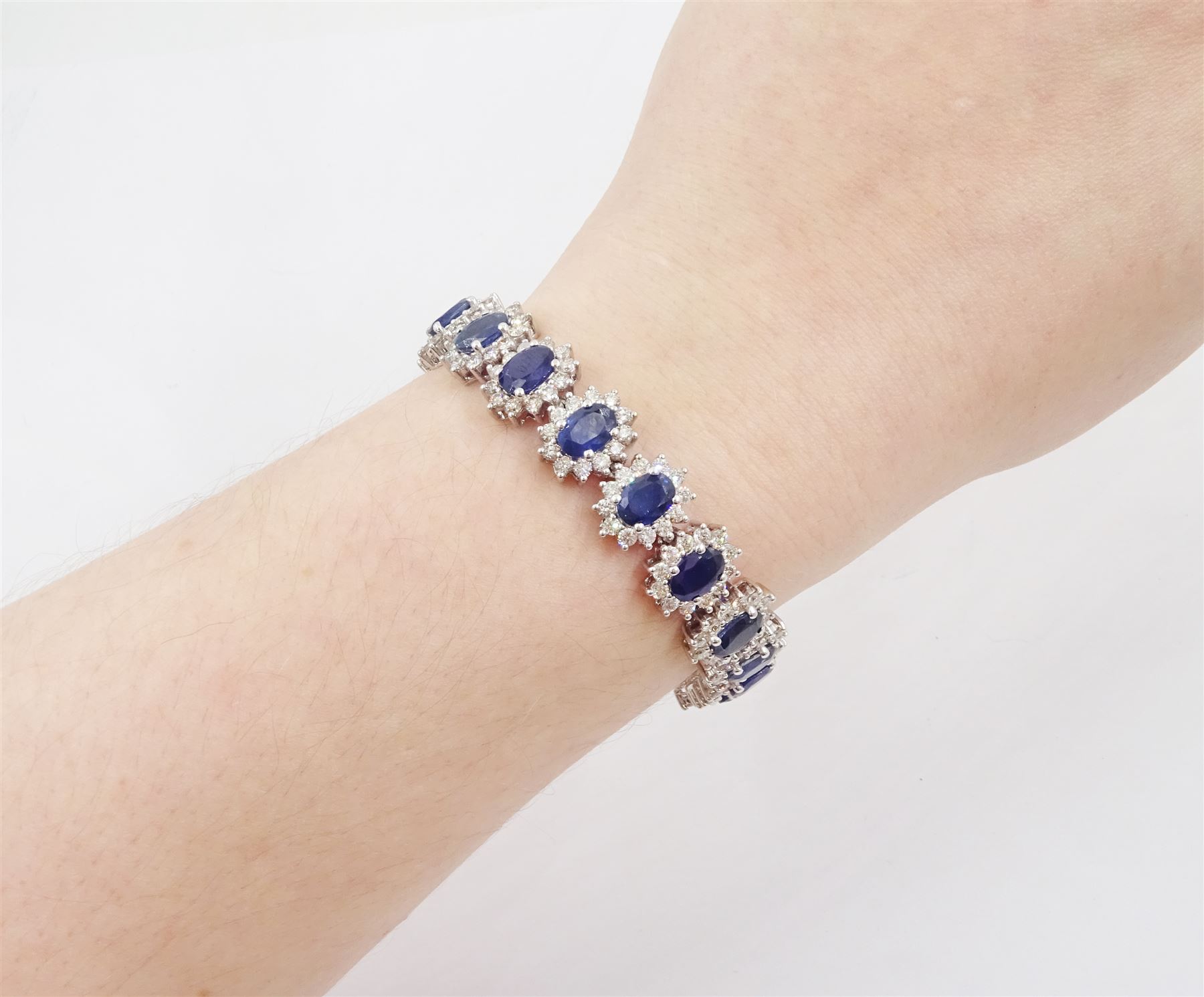 18ct white gold sapphire and diamond bracelet, nineteen clusters each set with a single oval cut sapphire and round brilliant cut diamond surround, stamped 750, total sapphire weight 18.20 carat, total diamond weight 6.38 carat