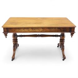 Mid Victorian walnut library table, plain top of rectangular form with moulded edge above frieze fitted with opposing drawers, table supported on a pair of turned and hexagonal carved baluster end standards, united by a turned stretcher terminating in scrolling sabre legs carved with acanthus and floral details, resting on ceramic castors, circa 1860