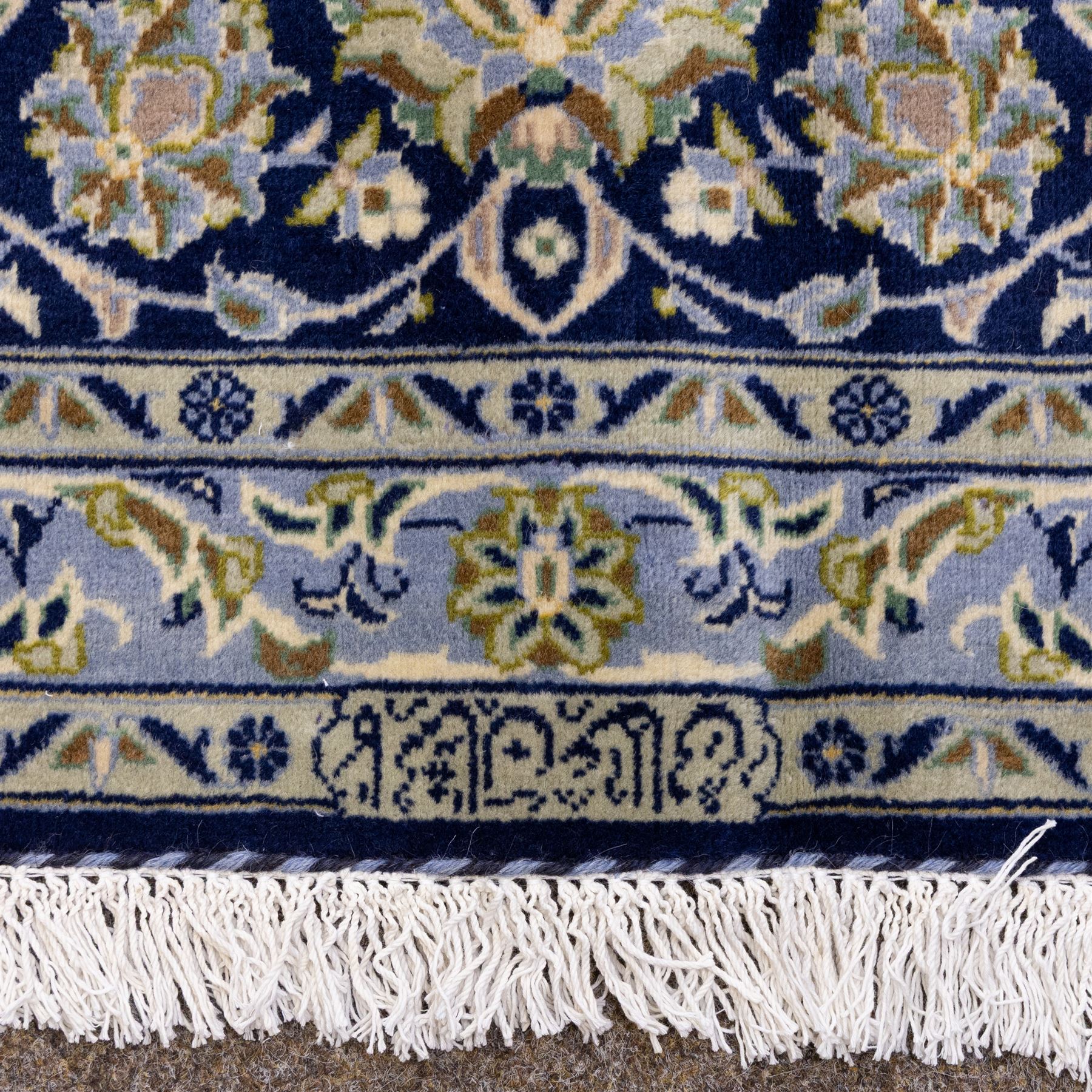 Central Persian Kashan hand-knotted rug, deep blue all-over field, finely decorated with dense scrolling floral sprays, palmettes, and flowering vines in ivory, soft gold, and pale green tones, enclosed by a multi-band floral border with corresponding guard stripes, with cotton fringe ends, signed Shah Abassi Workshop 