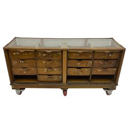 Early 20th century oak framed and glazed haberdashery / shop display cabinet, fitted with sixteen drawers (three missing), on later casters