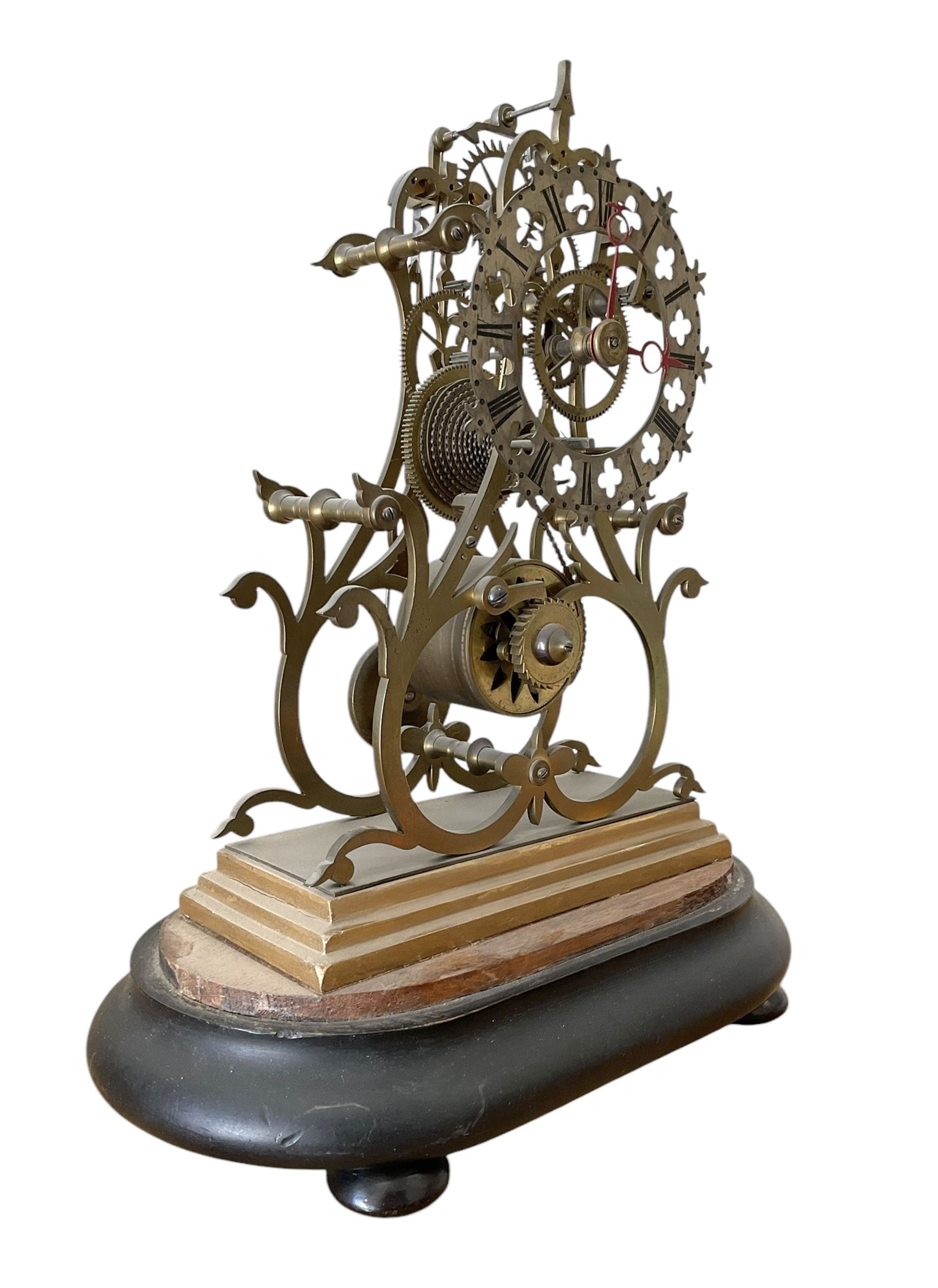 English-Late 19th century 8-day Skeleton clock on an oval ebonised base c1880, with pierced brass plates and silvered chapter ring, Roman numerals and gothic trefoil hands, chain driven five-pillar fusee movement and pierced mainspring barrel cap, timepiece movement with key and pendulum. 