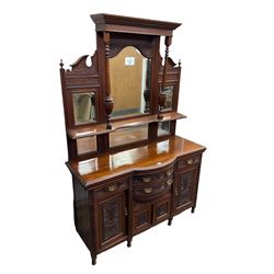 Edwardian walnut sideboard, projecting cornice supported by turned supports, the back fitted with three bevelled mirrors beneath fluted and flowerhead carved friezes, the lower section with four drawers and four panelled cupboard doors carved with foliate and urn designs, fluted uprights on turned feet