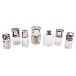 Seven glass scent bottles with silver covers, to include a Victorian example with clear glass cylindrical body, the plain hinged silver cover with engraved monogram, hallmarked Sampson Mordan & Co, London 1888, a similar Edwardian example with internal glass stopper, hallmarked Chester 1905, makers mark worn and indistinct, a Victorian example with cylindrical cut glass body and hinged foliate embossed cover, hallmarked Birmingham 1897, makers mark indistinct, possibly Akers & Co, etc.
