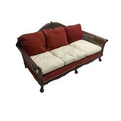 Early 20th century bergère three seat settee, shaped shell carved cresting rail, double caned back and sides, scrolled upright arms and shaped apron carved with shell and foliage, on hairy paw carved feet