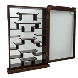 Chinese hardwood wall hanging curio cabinet, the mirror interior fitted with stepped shelves, enclosed by single glazed doors, decorated with carved scrolling foliage 