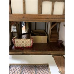 Gerry Welch for Manorcraft Tudor style wooden doll's house, of three-storey multi gabled form with mock beam and plaster walls and simulated leaded glass windows under a felt tiled roof, boarded floors and stairs to each room, curtains to most windows, front entrance door, rear door and single storey extension for kitchen. Furniture includes fitted floral bathroom suite to top floor, well stocked Welsh dresser with copperware etc, tapestry style wall hangings, knole settee, tin bath, metal range, fire-surround, wooden three-piece suite etc; on shaped cobbled base W91cm D61cm H91cm