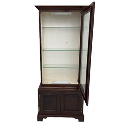 Mahogany display cabinet with hidden compartment, projecting cornice over single glazed door enclosing glass shelves, double panelled cupboard below, the interior with button releasing sliding back compartment, on bracket feet