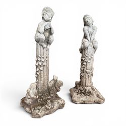 Pair of weathered composite stone garden figures, modelled as a girl and a young satyr playing the panpipes seated on column supports, the fluted columns with climbing ivy vines and surmounted animal, butterfly and other zoomorphic motifs