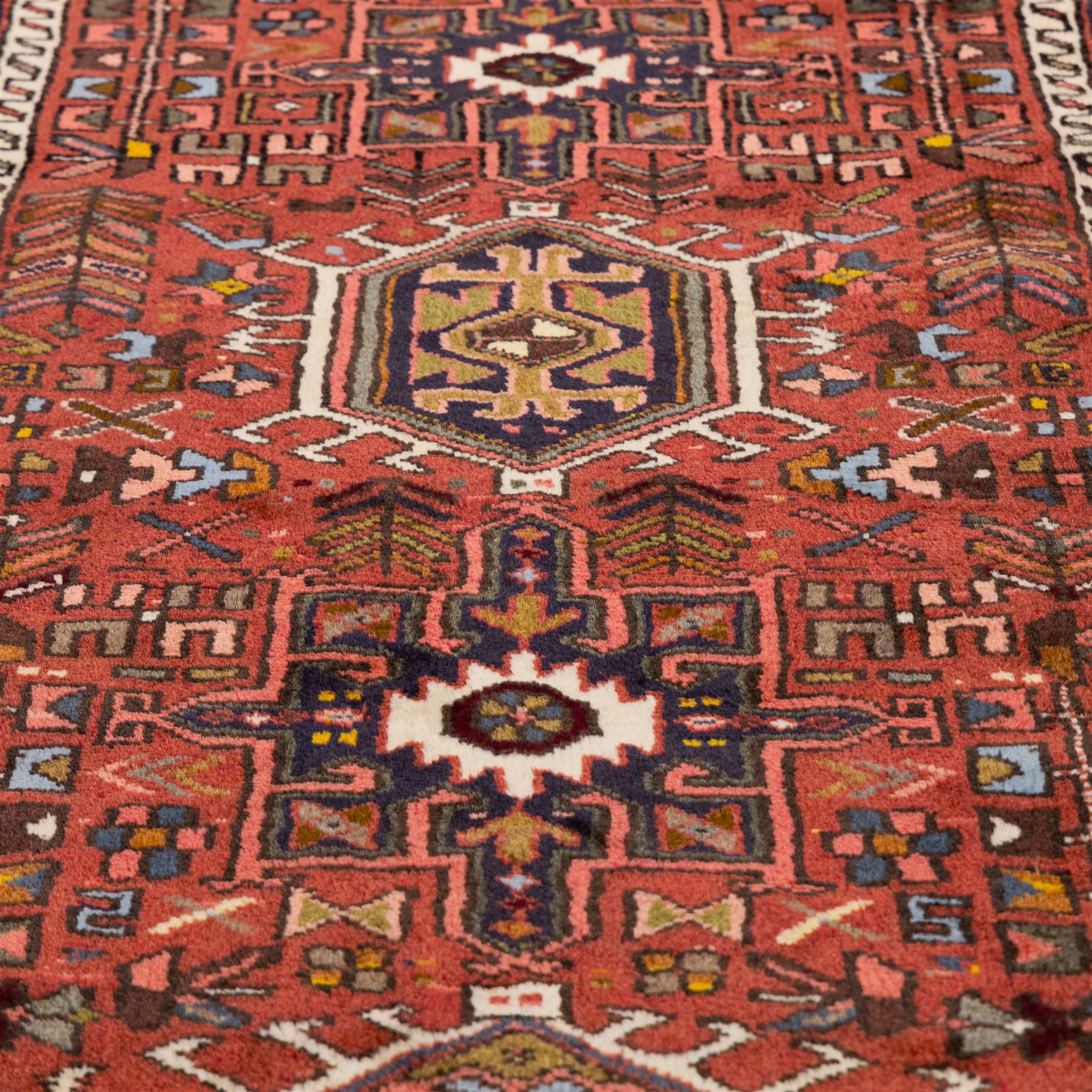 North West Persian Heriz hand-knotted runner, terracotta field decorated with a series of large angular medallions with stylized geometric motifs, surrounded stepped devices, and stylized trees within narrow geometric border, and polychromed edge, cotton fringe ends 