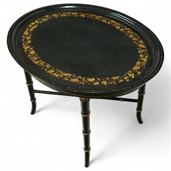 Regency style oval toleware tray table, the black lacquered top with gilt floral decoration, on ebonised faux bamboo frame with stretcher supports