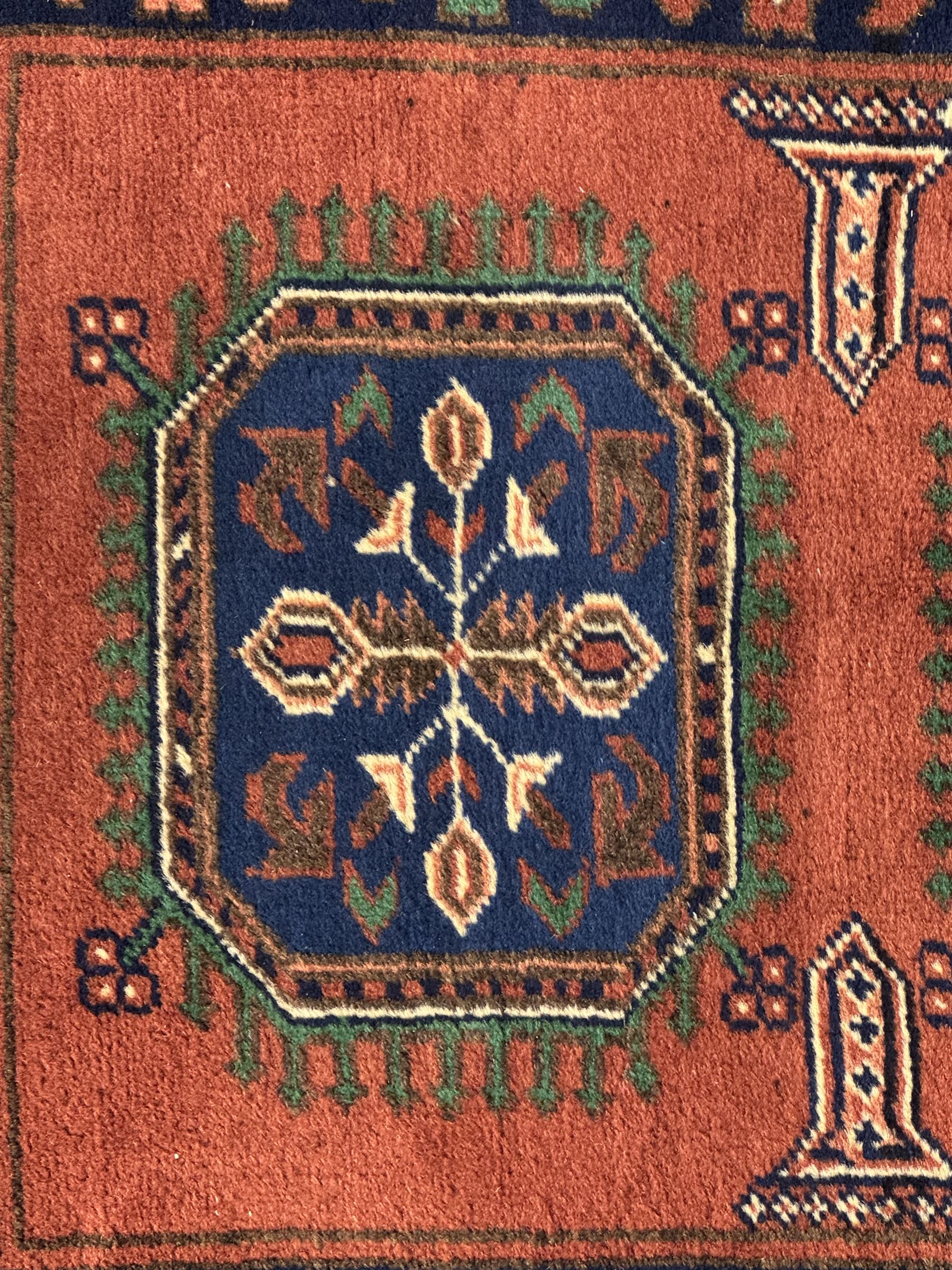 Late 20th century Afghan style ground runner, woven with a repeating panel design along a terracotta field and indigo grounds, framed by multiple narrow borders, and finished with fringed ends