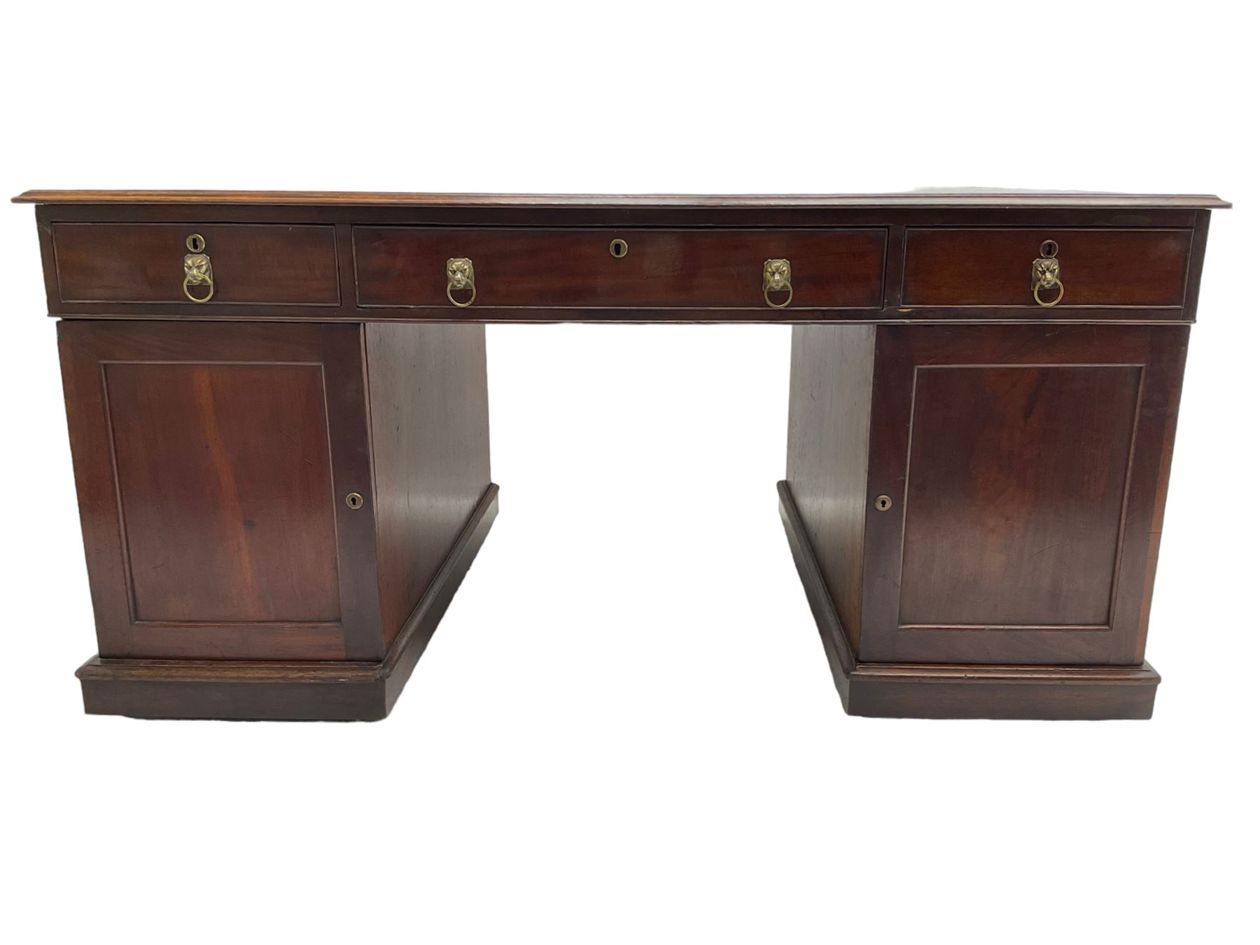 George III mahogany twin pedestal partners desk, rectangular top with moulded edge and an inset green tooled leather writing surface with Greek key design border, fitted with three cock-beaded frieze drawers to each side, each pedestal with three graduating drawers with an opposing panelled cupboard enclosing a single shelf, the facias fitted with brass lion mask plates with ring handles, the lower moulded edge over a plinth base and castors, London furniture dealers label to interior of drawer inscribed 'J. Webb, Office Furniture 323, Gray's Inn Road, King's Cross'  H75cm  W153cm  D97cm