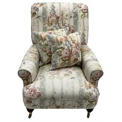 Victorian design armchair, rolled back and arms, upholstered in floral pattern fabric with two scatter cushions, on turned front feet with brass cups and castors
