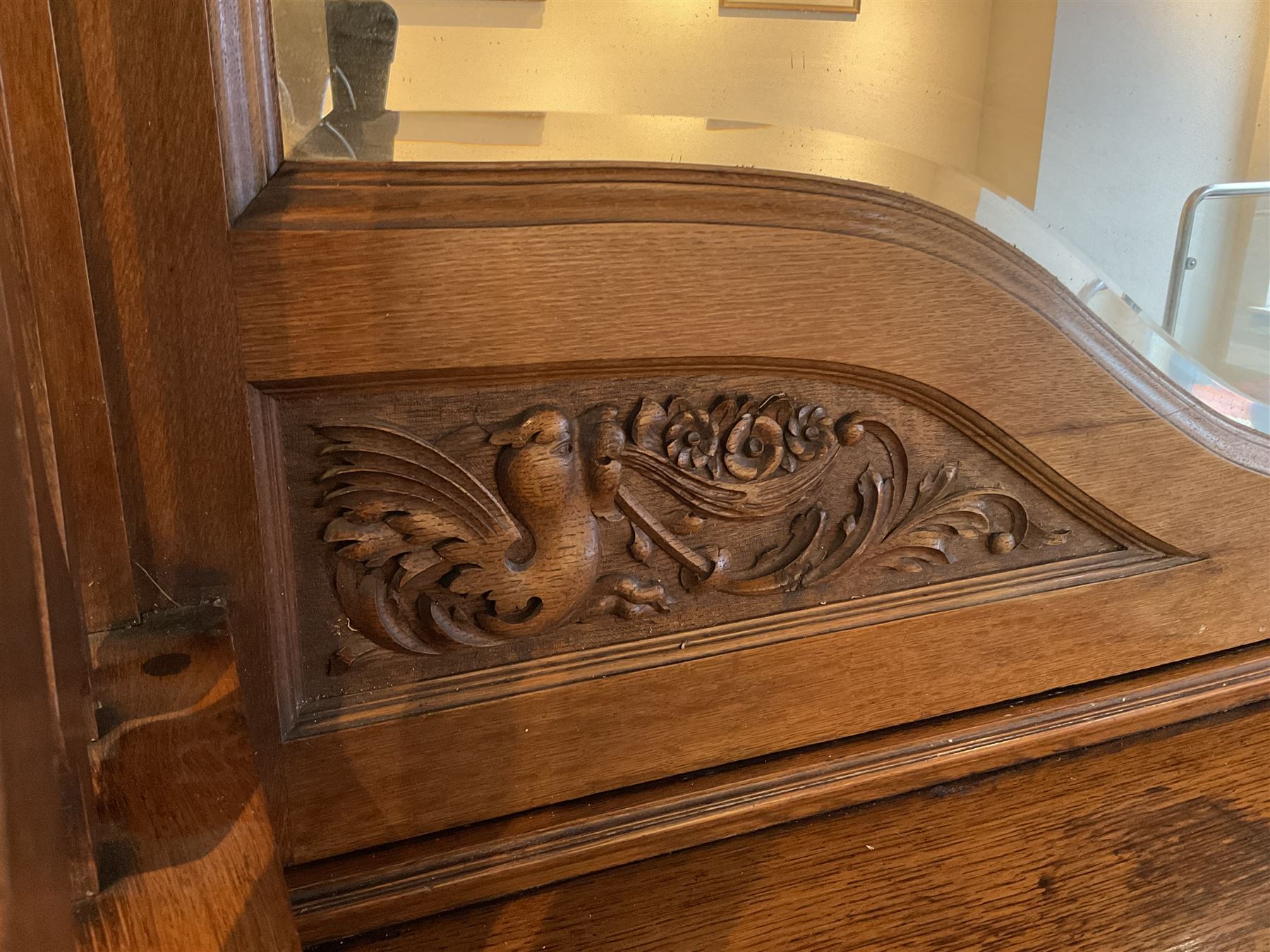 Late 19th century Arts & Crafts period oak mirror back sideboard, shaped bevelled mirror back carved with foliate scrolls and flower heads, down swept supports with elongated club-shaped uprights, moulded rectangular top over two drawers and three cupboards, the drawer fronts with copper handles decorated with sailing ships, panelled doors carved with mythical beasts, flowerheads and foliage, on moulded block feet