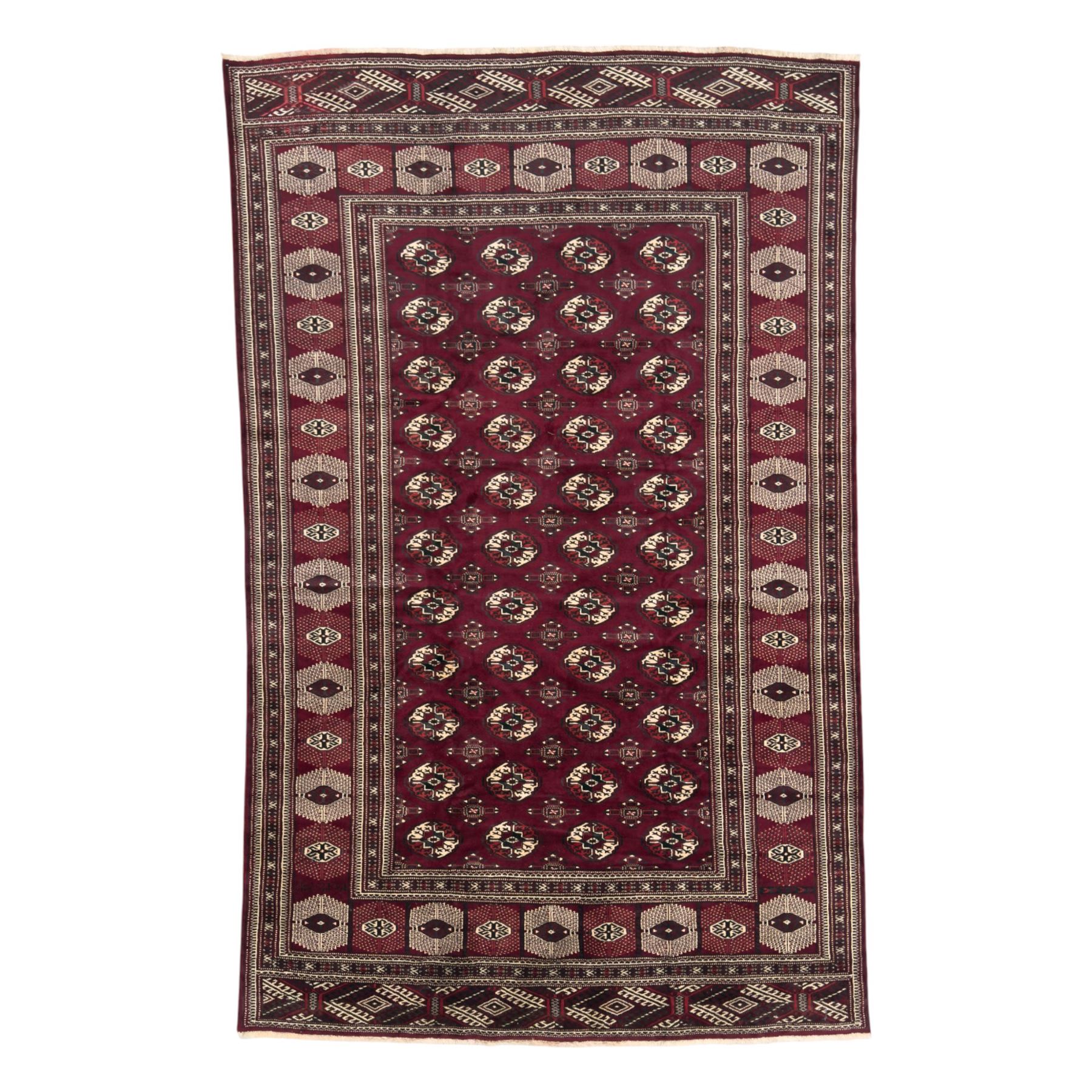 Northeastern Persian Yamut  hand-knotted carpet, the rich burgundy field with repeating rows of stepped gul motifs in cream and black, enclosed by multiple linear and geometric borders with hooked motifs and diamond medallions