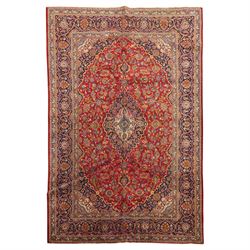 Persian Kashan hand-knotted carpet, madder red ground centred by shaped dark navy, ivory a...