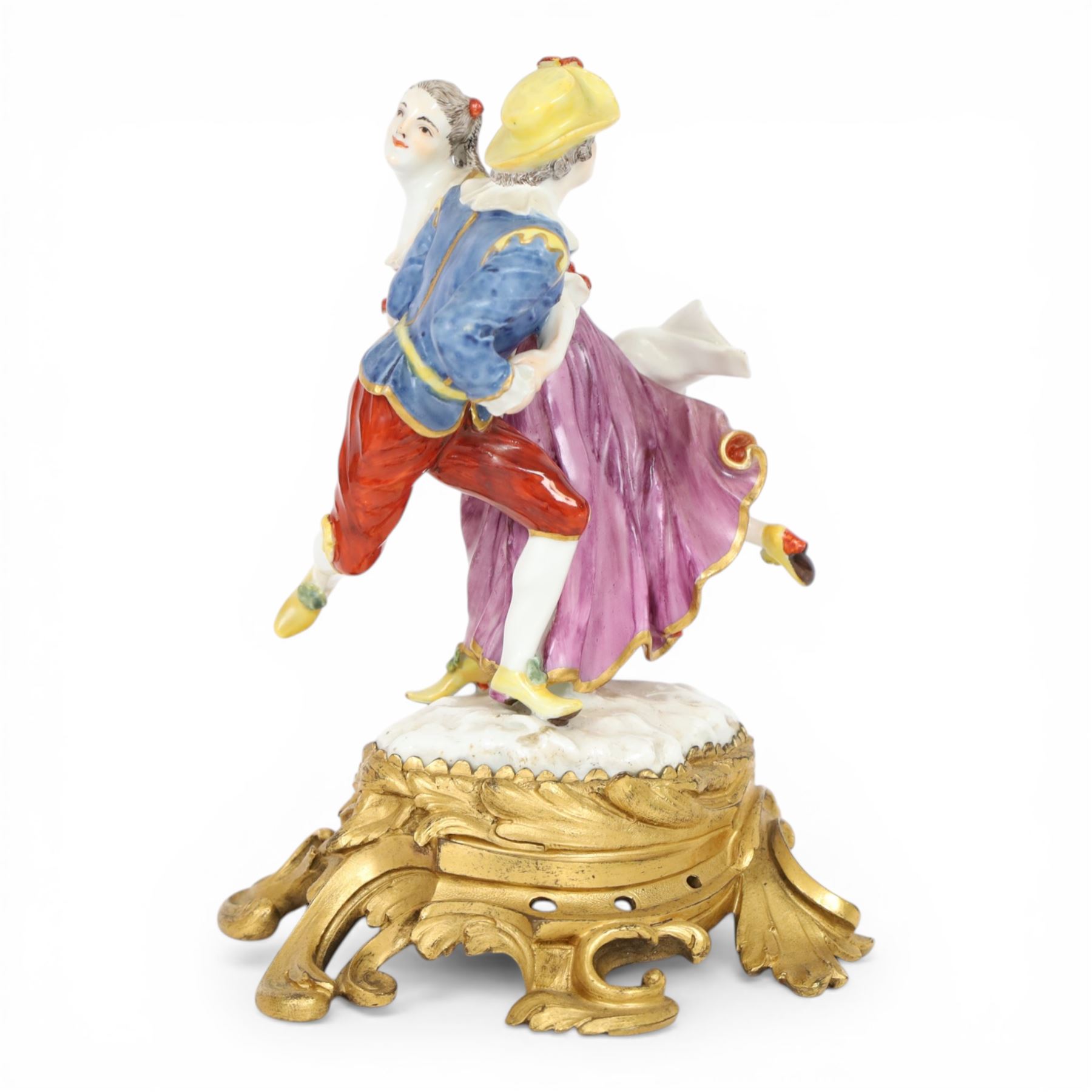 Mid 18th century Meissen figure group, The Tyrolean Dancers, circa 1740, modelled as two swirling figures with their arms linked, he in yellow hat with red rosette, blue jacket, red breeches with red rosette, and yellow shoes with green rosette, she in white blouse with red ribbons, yellow and red bodice, white apron over puce skirt and yellow shoes with green rosettes, her hair fashioned into two plaits secured by red ribbon, upon a shaped mound base, within a scrolling gilt metal mount, with blue crossed swords mark to base, overall H19cm
