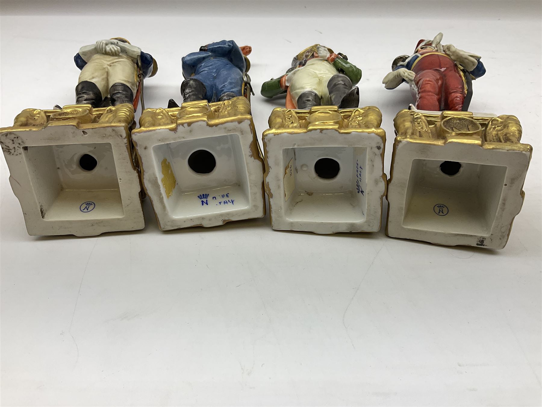 Group of seven Capodimonte figures of soldiers, to include four Bruno-Merli examples including Officer of the 12th Lancers 1820 and Captain of the 18th Hussars 1815, both raised upon ornate gilt plinths bearing British monarch motto in Latin 'Dieu et mon droit', and three further similar, all with crowned N mark beneath, tallest H32cm