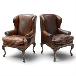 Pair of quality Queen Anne design mahogany framed wingback armchairs with matching footstools, the high sprung winged backs over rolled arms with studwork, raised on elegant reeded scroll carved cabriole supports, upholstered in deep chocolate brown leather (W82cm D75cm H112cm), the footstools with ovoid padded seat over studwork and moulded lower rail and cabriole supports (W65cm D42cm H48cm)
