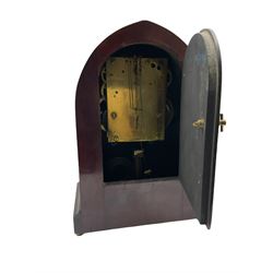A late 19th century American  mantle clock in a “Lancet” case manufactured by the  Gilbert Clock Factory, Connecticut,  mahogany veneered case with an oval inlay, satinwood stringing to the edge and two recessed brass pillars, on a moulded plinth with four bun feet, enamel dial with upright Arabic numerals and spade hands, fast/slow regulation, with a convex glass and spun brass bezel, eight-day movement striking the hours and half hours on a coiled gong. No pendulum.