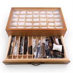 Large wooden watch display case, with glazed lid and spaces for thirty five watches, with drawer beneath containing a collection of leather, metal and other watch straps