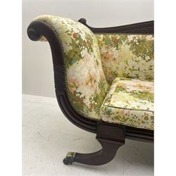 Regency period mahogany settee, scroll and lobe carved cresting rail, upholstered in floral patterned fabric with squab cushion, double scrolled and shaped ends, splayed moulded supports with brass cups and castors
