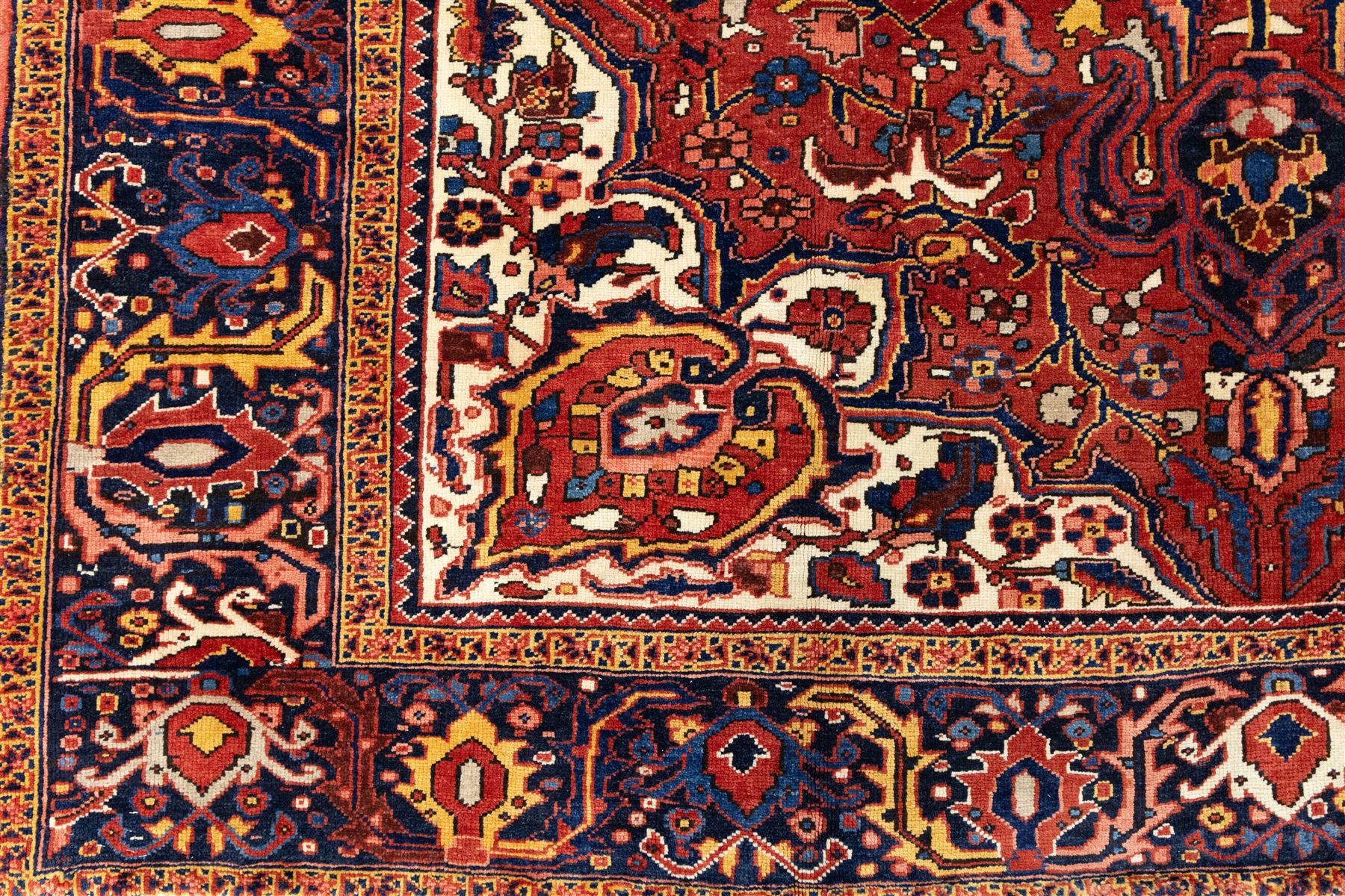 North West Persian Ahar hand-knotted carpet, red field with large central angular star medallion with stepped outlines and radiating geometric motifs surrounded by stylized floral and serrated leaf forms, enclosed by a deep blue main border decorated with angular palmettes and rosettes flanked by multiple guard stripes, with cotton fringe ends 