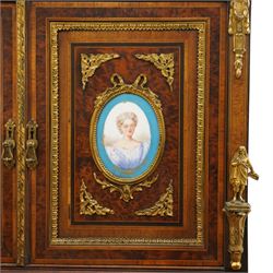 Fine late 19th century Aesthetic Movement ebony and amboyna cabinet on stand with parcel-gilt detail, the moulded cornice with pierced gilt-brass three-quarter gallery above a pair of panelled doors centred by oval porcelain portrait plaques within gilt-metal ribbon-tied frames, the doors further enriched with gilt-metal foliate mounts and flanked by classical figural terms, enclosing a shelved interior, the projecting lower section with amboyna top above a frieze drawer set with a series of floral porcelain roundels within pierced gilt-metal mounts and a central oval floral plaque, raised on turned and fluted supports with gilt-heightened detail, the mirrored back behind two amboyna shelves with pierced gilt-brass galleries, on turned feet