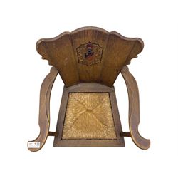Pair of Arts and Crafts oak armchairs each with shaped backrest centred by polychrome painted crest, rush seat over straight square legs united by shaped central stretcher