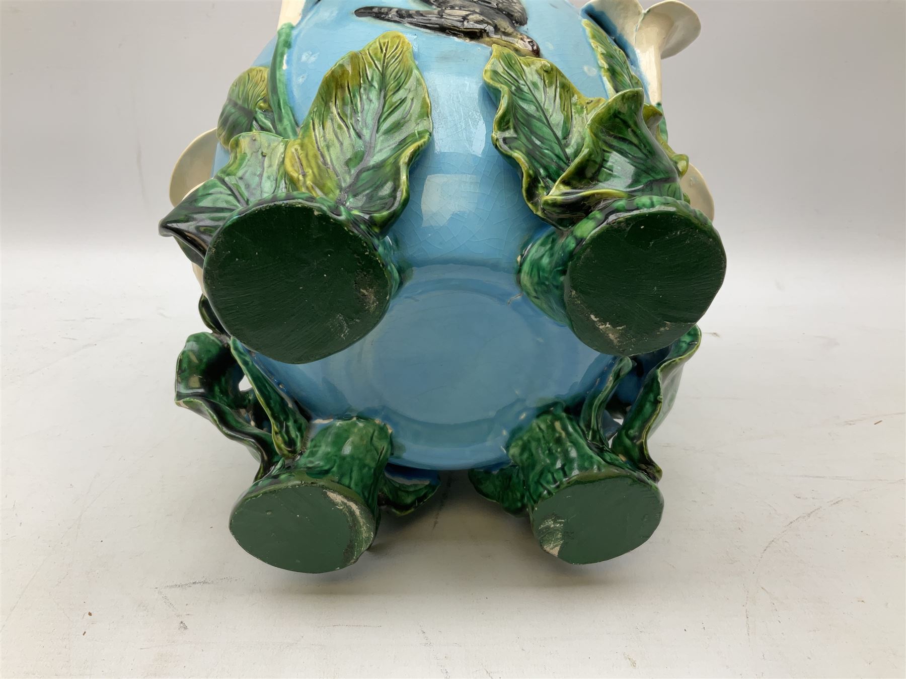 George Jones style majolica jardiniere of globular form, supported on four feet formed from modelled lily leaves growing up the side of the pot, with swallows flying amongst the white lily flowers, all set against a blue ground, with a pink interior, H27cm