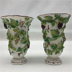 Pair of 19th century vases, each decorated in relief with fruiting vines, upon a white ground, hand painted with floral sprigs and insects, with lobed rim and upon stepped base, H13cm