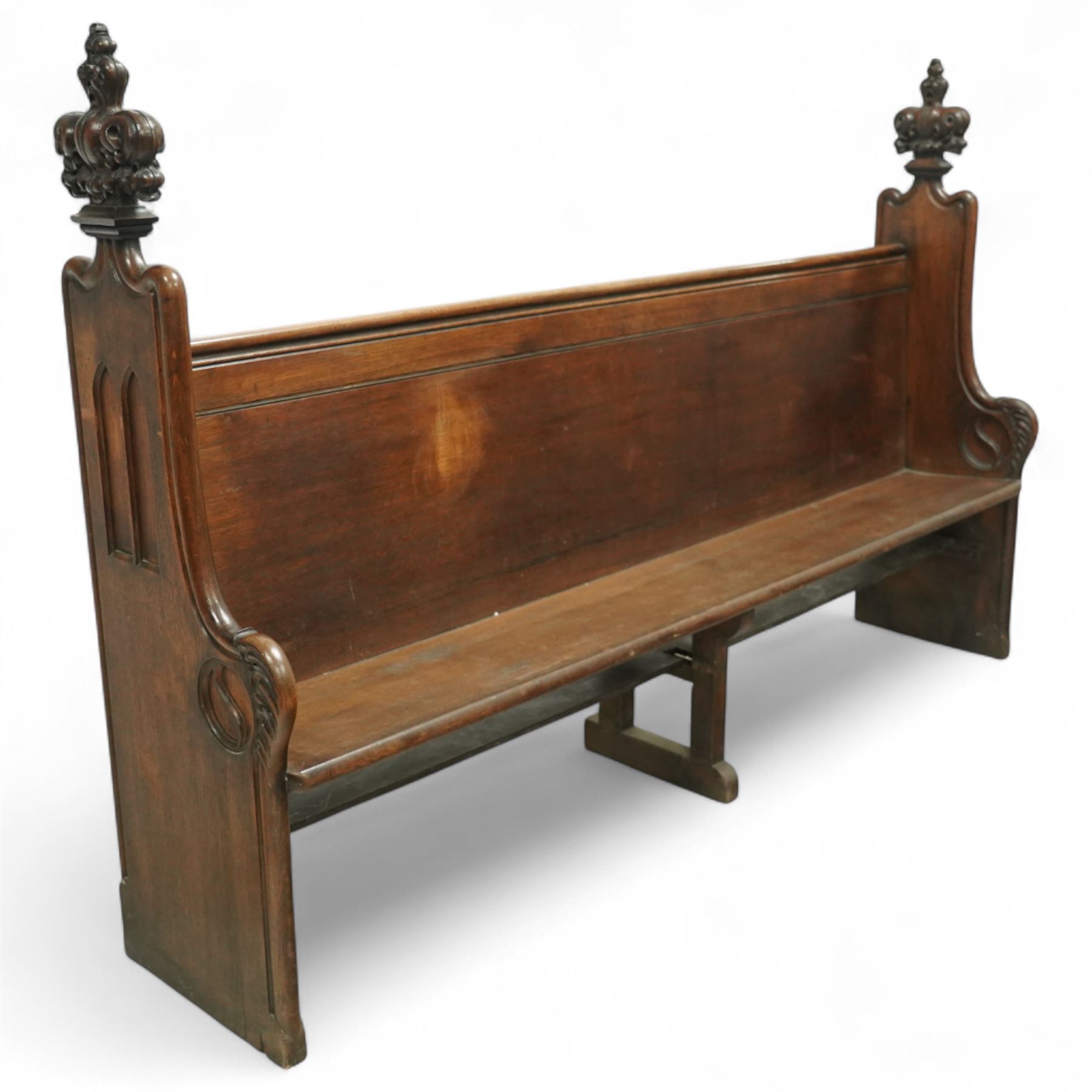 Late 19th century Gothic revival oak church pew, with high backrest framed by carved stylised cross panels and crown-topped finials, shaped end panels with scroll detailing, on block end supports and central stretcher, with later padded seat cushion