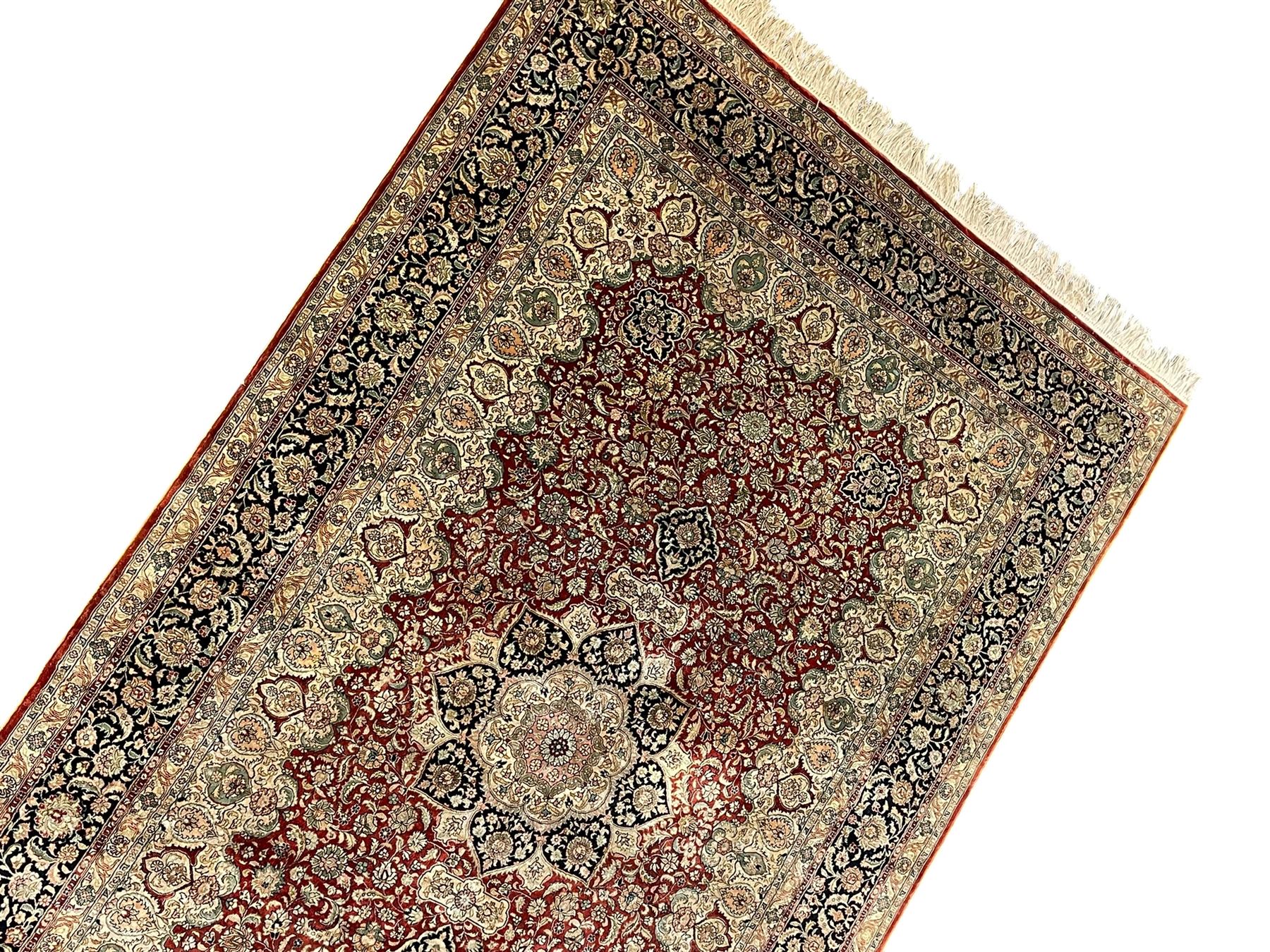 Persian silk finely knotted rug, central floral rosette medallion surrounded by curling branches decorated with palmettes, repeating pattern borders decorated with stylised plants and trailing leafy branches  
