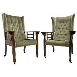 Pair of Arts and Crafts period oak framed wingback armchairs, upholstered in slung buttoned covers, shaped extending armrests on tapering supports terminating to spade feet, on castors  